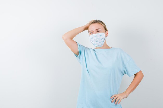 Jeune femme en t-shirt, masque tenant la main sur la tête et à l'oubli