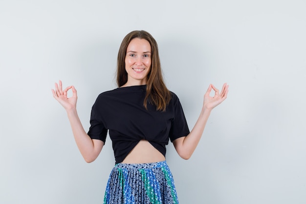 Jeune femme en t-shirt noir et jupe bleue debout dans le geste de méditation et à la recherche attrayante