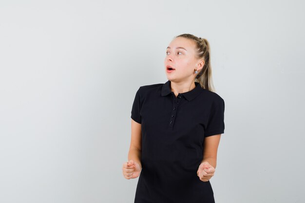 Jeune femme en t-shirt noir serrant ses bras comme pompe de poing et à l'optimiste