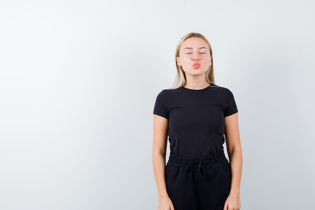 Jeune femme en t-shirt, pantalon envoyant un baiser avec des lèvres boudeuses et jolie vue de face.