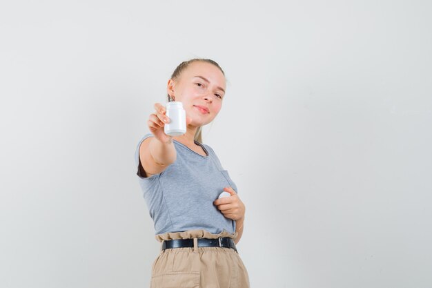 Jeune femme en t-shirt et pantalon montrant une bouteille de pilules et à la confiance