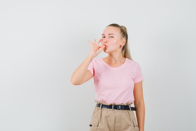 Jeune femme en t-shirt, pantalon montrant un geste délicieux et à la ravie, vue de face.