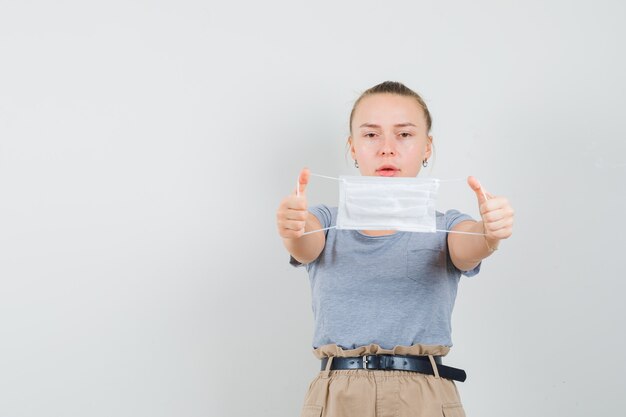 Jeune femme en t-shirt et pantalon montrant un masque médical et à la prudence