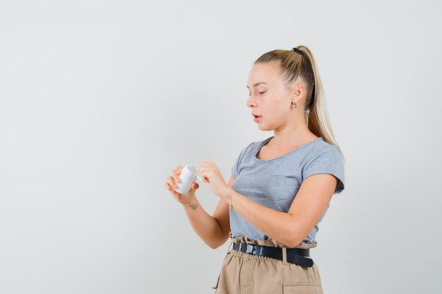 Jeune femme en t-shirt et pantalon ouvrant la bouteille de pilules et à la prudence