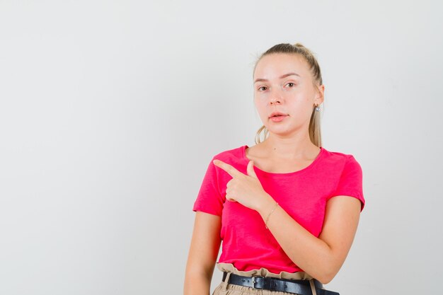 Jeune femme en t-shirt et pantalon pointant vers le coin supérieur gauche