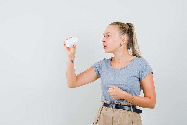 Jeune femme en t-shirt et pantalon à la recherche en bouteille de pilules et à la recherche concentrée