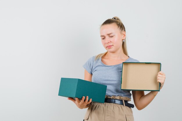 Jeune femme en t-shirt et pantalon à la recherche dans la boîte actuelle et à la déception