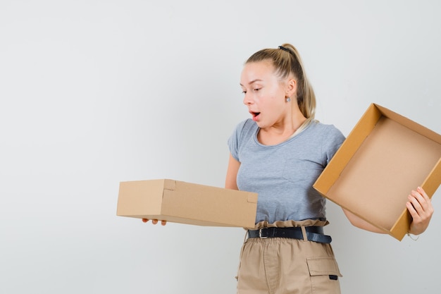 Jeune femme en t-shirt et pantalon à la recherche dans une boîte en carton et à la surprise