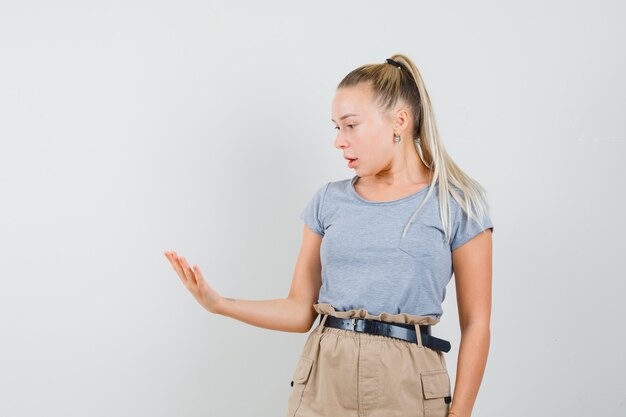 Jeune femme en t-shirt et pantalon regardant sa paume vide et à la surprise