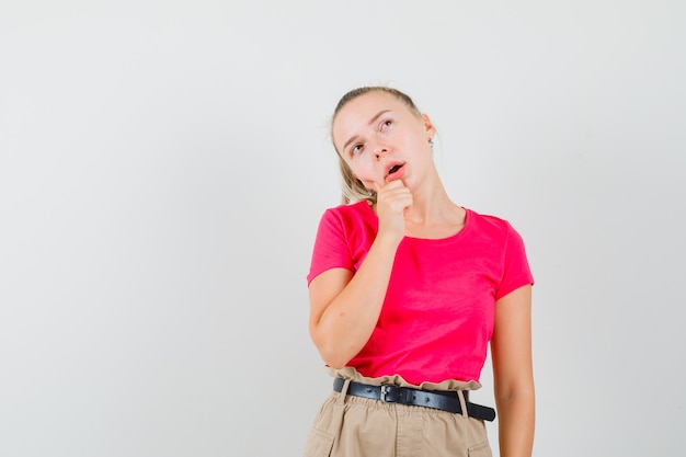 Jeune femme en t-shirt et pantalon tenant son menton et à la rêveuse