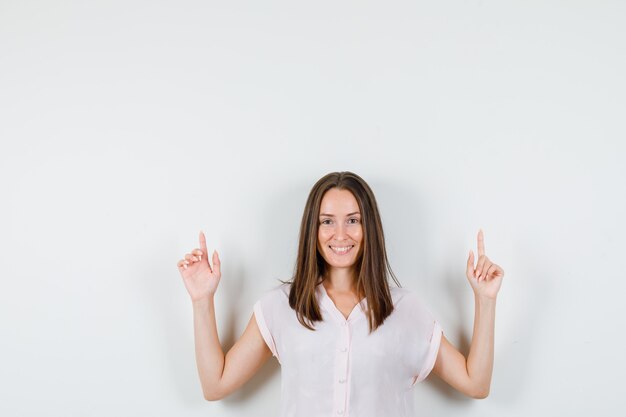 Jeune femme en t-shirt pointant vers le haut et à la joyeuse vue de face.