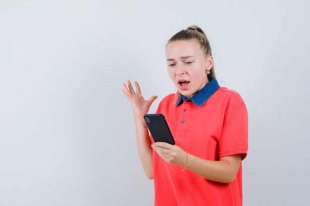 Jeune femme en t-shirt à la recherche de téléphone mobile et à l'excitation