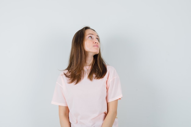 Jeune femme en t-shirt rose regardant vers le haut et à la recherche focalisée, vue de face.