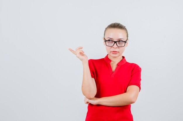 Jeune femme en t-shirt rouge, lunettes pointant vers le côté et à la recherche concentrée