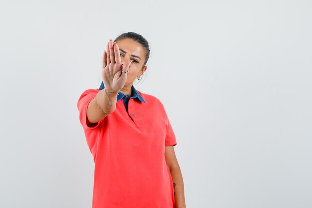 Jeune femme en t-shirt rouge montrant le panneau d'arrêt et à la grave, vue de face.