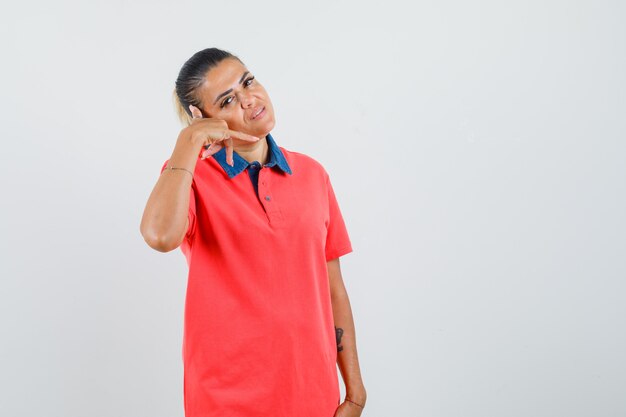 Jeune femme en t-shirt rouge qui s'étend de la main comme parler au téléphone et à la vue de face, heureux.