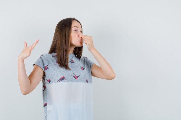 Jeune Femme En T-shirt Se Pincer Le Nez à Cause De La Mauvaise Odeur Et à La Dégoûté, Vue De Face.