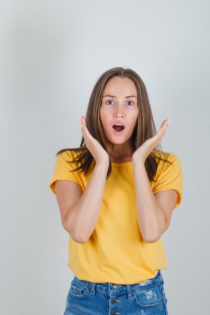 Jeune femme en t-shirt, short main dans la main près du visage et à la surprise