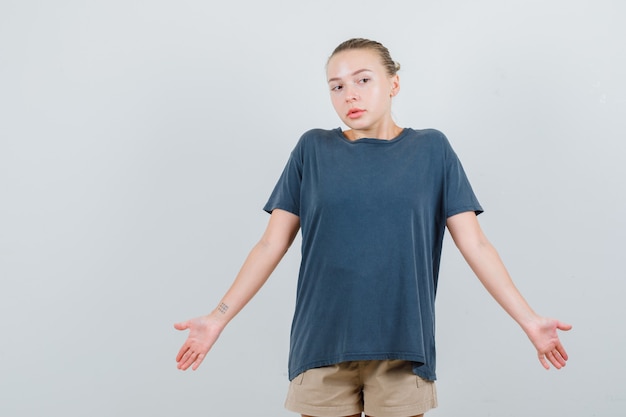 Jeune femme en t-shirt, short montrant un geste impuissant en haussant les épaules et à la confusion