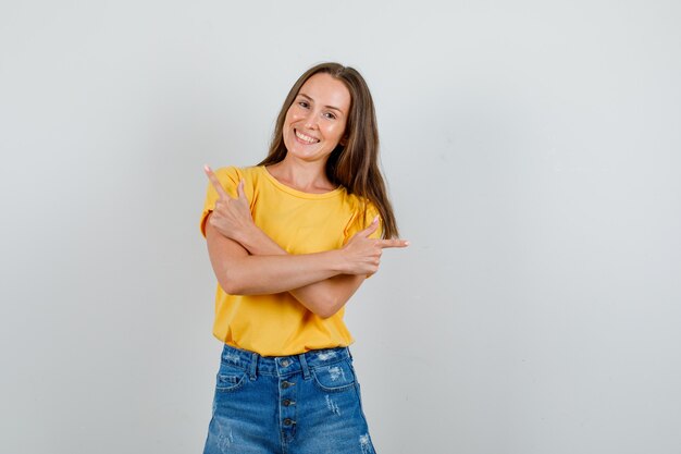 Jeune femme en t-shirt, short pointant vers le côté avec le geste du pistolet et à la bonne humeur