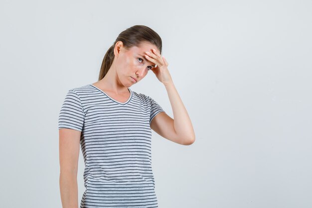 Jeune femme en t-shirt tenant les doigts sur le front et les tempes et l'air fatigué, vue de face.