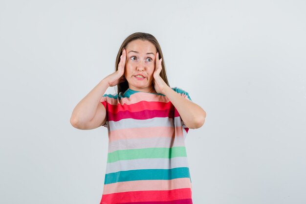 Jeune femme en t-shirt tenant les doigts sur les tempes et à la perplexité, vue de face.