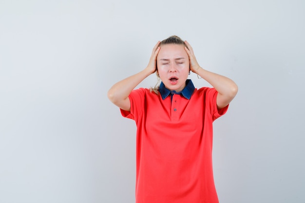 Jeune femme en t-shirt tenant la main à la tête et à la déprimée, vue de face.