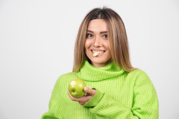 Jeune femme en t-shirt vert mangeant une pomme.