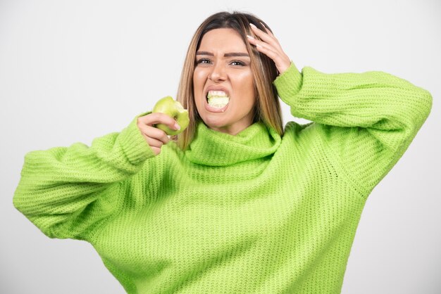 Jeune femme en t-shirt vert mangeant une pomme.