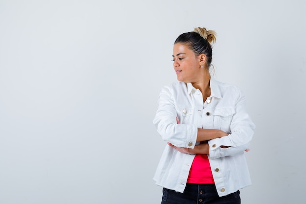 Jeune femme en t-shirt, veste blanche debout avec les bras croisés et l'air confiant, vue de face.