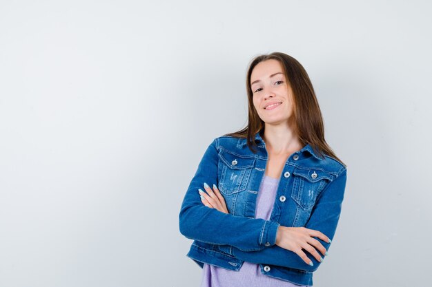 Jeune femme en t-shirt, veste debout avec les bras croisés et l'air joyeux, vue de face.