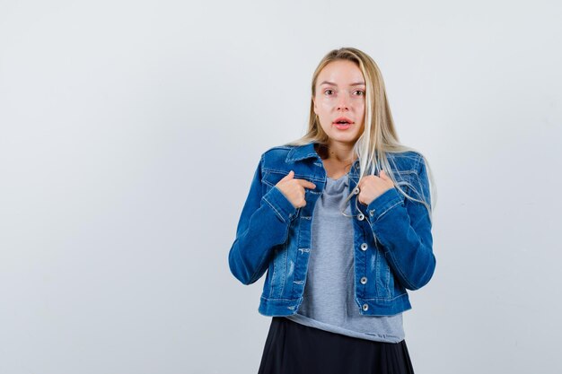 Jeune femme en t-shirt, veste en jean, jupe se pointant et semblant étonnée