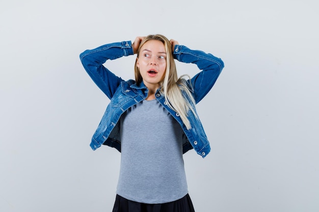 Jeune femme en t-shirt, veste en jean, jupe tenant la main sur la tête et l'air étonné