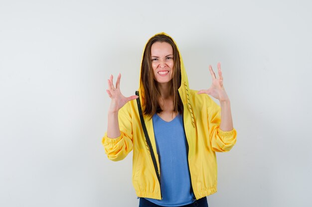 Jeune femme en t-shirt, veste levant les mains de manière agressive et semblant excitée, vue de face.