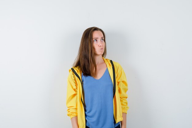 Jeune femme en t-shirt, veste en levant et regardant réfléchie, vue de face.