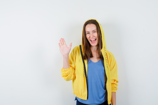 Jeune femme en t-shirt, veste montrant la paume et l'air heureux, vue de face.