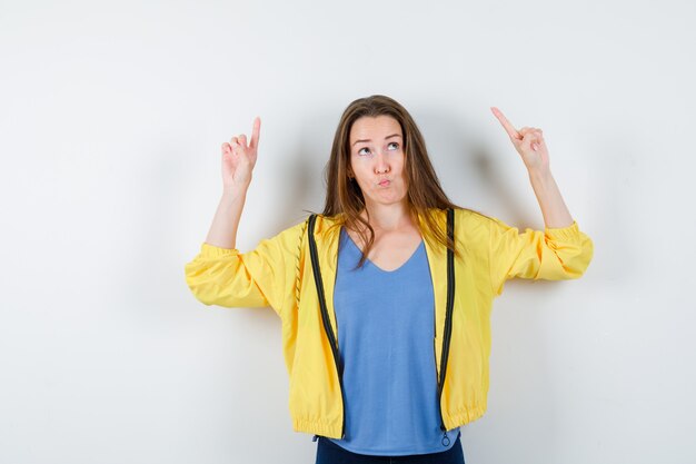 Jeune femme en t-shirt, veste pointant vers le haut et hésitante, vue de face.