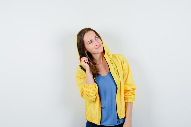 Jeune femme en t-shirt, veste posant en levant les yeux et l'air rêveuse