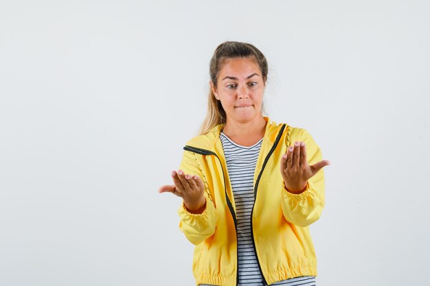 Jeune femme en t-shirt, veste regardant ses paumes et regardant pensif, vue de face.