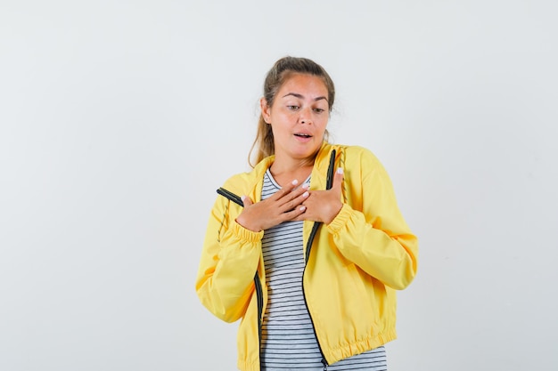 Jeune femme en t-shirt, veste tenant les mains sur la poitrine et à la recherche élégante, vue de face.