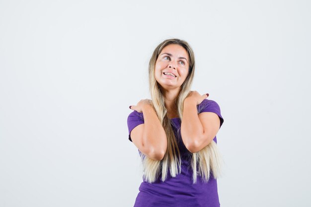 Jeune femme en t-shirt violet tenant les mains sur les épaules et à la belle vue de face.