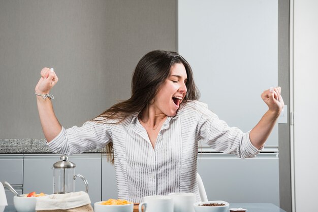 Jeune femme, à, table petit déjeuner, bâiller, et, s&#39;étendant mains