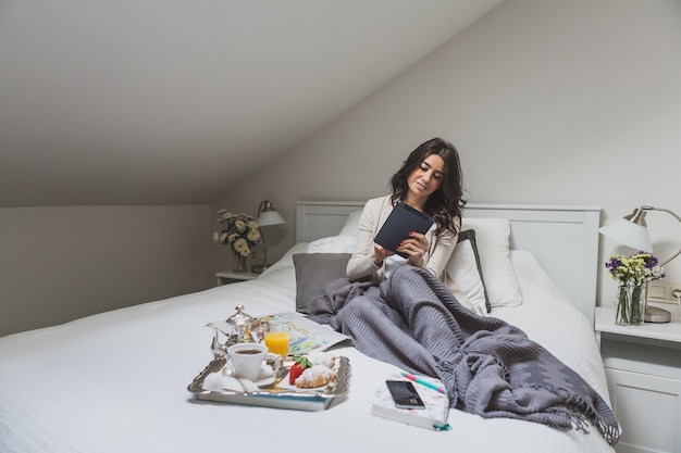 Jeune femme avec tablette assis sur le lit