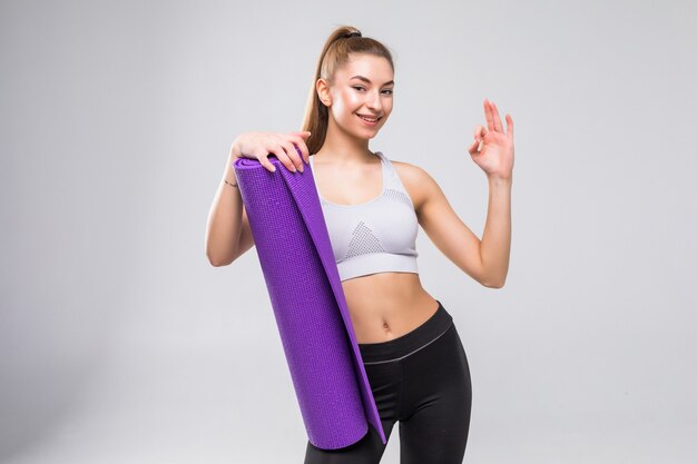 Jeune femme avec tapis de yoga montrant signe correct isolé sur blanc