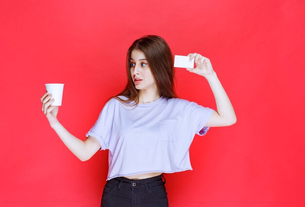 jeune femme avec une tasse de boisson présentant sa carte de visite.