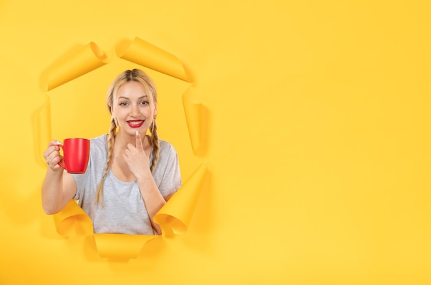 Jeune femme avec une tasse de thé sur une surface jaune déchirée