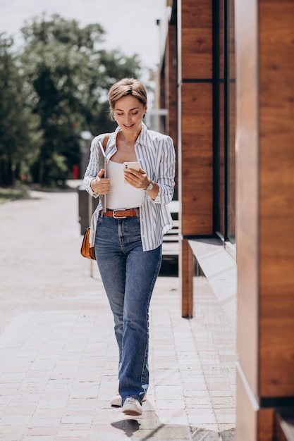 Jeune femme avec téléphone et ordinateur marchant à l'extérieur de la rue