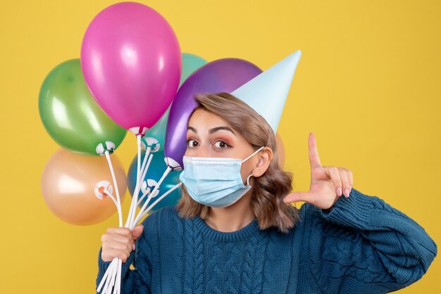 jeune femme tenant des ballons colorés en masque sur jaune