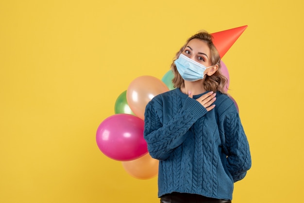 jeune femme tenant des ballons colorés en masque sur jaune