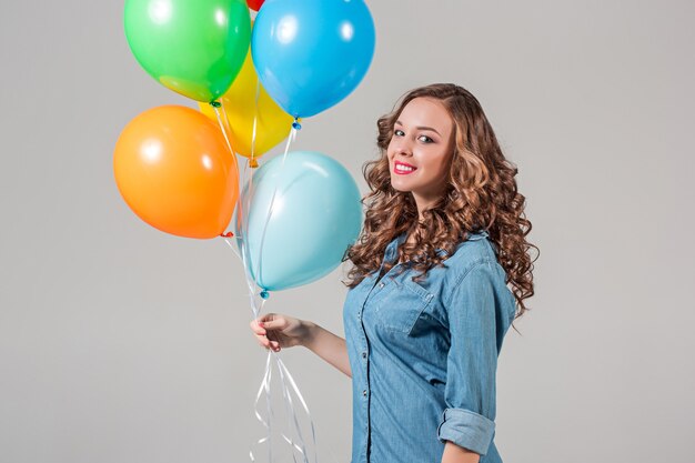 Jeune femme tenant des ballons colorés sur mur gris studio